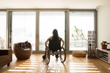 Young disabled woman in wheelchair at home, rear view. - Powered by Adobe