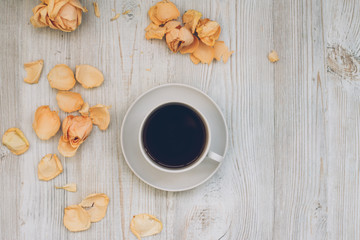Morning coffee cup on white wooden desk with rose petals, romantic background