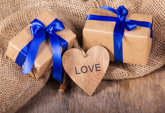 Gift boxes from recycled paper decorated with blue satin bow. Wooden Valentine on the old wooden background. Valentine's Day.