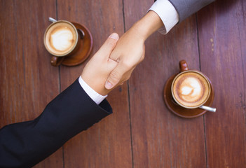 Business talk and hands shake at a coffee shop with two cups of latte