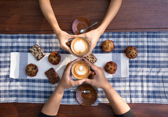 Coffee and cake with hands holding cups of hot latte decorated with muffin and brownies