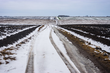 Hilly landscape with dirty country road between agricultural fields in central Ukraine at gloomy...