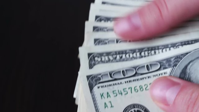 Women's hands holding a fan of hundred dollar bills and counts