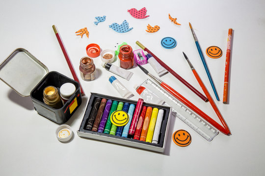Kids tools and items for painting and creative works with color paints brushes plasticine pastels and pencils on white table top.