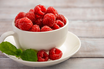 Ripe sweet raspberries in white cup on wooden table, selective focus, horizontal, close up, copy space.