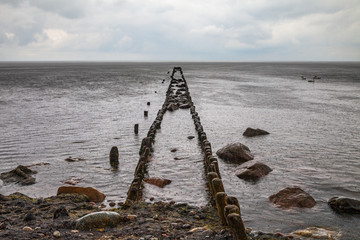Fototapeta premium Old broken pier at stone beach of the Baltic sea