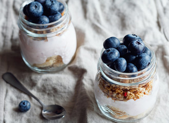 Close up of granola with fresh berries, raspberry yogurt and banana in glass jars on a rustic flax beige napkin