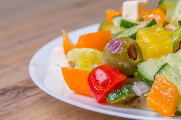 Greek salad in white glass dish plate, closeup from the side. Olives, tomatoes, paprika, bell pepper, cucumber, onion, feta cheese, olive oil. Standing at wooden background macro.