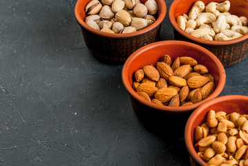 Four bowls with different nuts on a stone kitchen table: cashews, almonds, peanuts and pistachios, copy space, top view