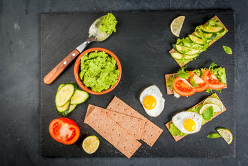 Healthy Eating, Diet sandwiches on gluten-free loaves - with guacamole, fresh vegetables (tomato, cucumber), egg, lime, lettuce and basil, On a stone (concrete) gray table, top view
