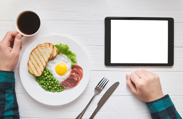 Healthy morning breakfast online shopping concept with tablet blank pure white screen for text or picture design. Man's hands with eggs, peas, bread and juice meal. Modern people lifestyle flat lay