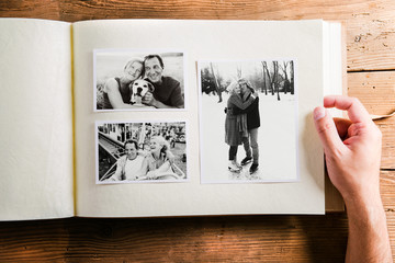 Hand holding photo album with pictures of senior couple. Studio  - obrazy, fototapety, plakaty