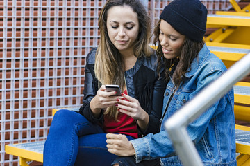 two mixed race female friends sitting and using a smartphone