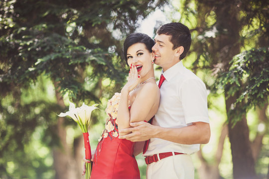 Groom with red tie hugs bride in red wedding dress