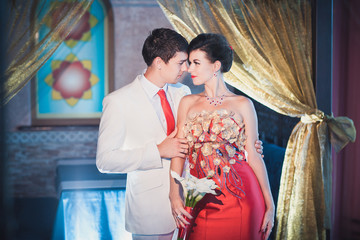 Red wedding, groom in white suit with red tie hugs bride in red wedding dress