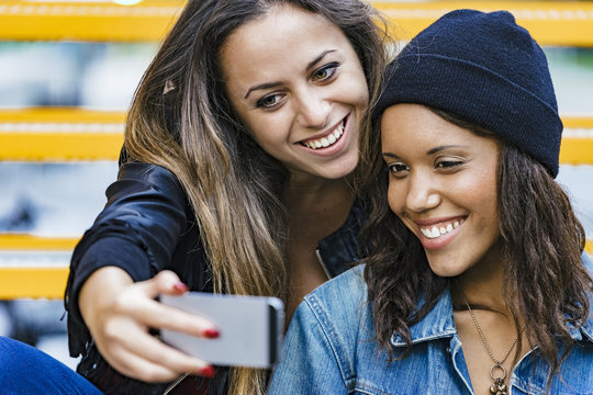 two female mixed race friends having a coffee and taking a selfie