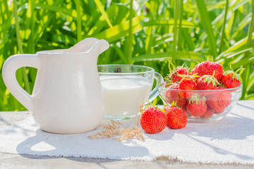 Миска с клубникой, чашка с молоком и кувшин на салфетке на деревянном столе