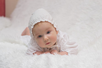 little girl in white dress and hat, after baptism, lying on his stomach on a white fur rug of white background three months © silentalex88