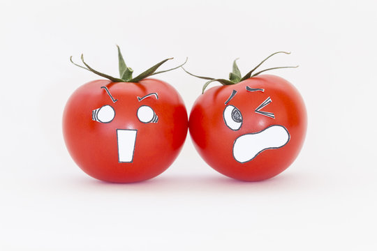 Two fresh red tomatoes with scared faces in front of white background