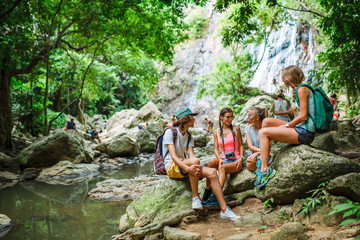 Obraz premium tourists sitting on rocks talking in front of jungle river with waterfall