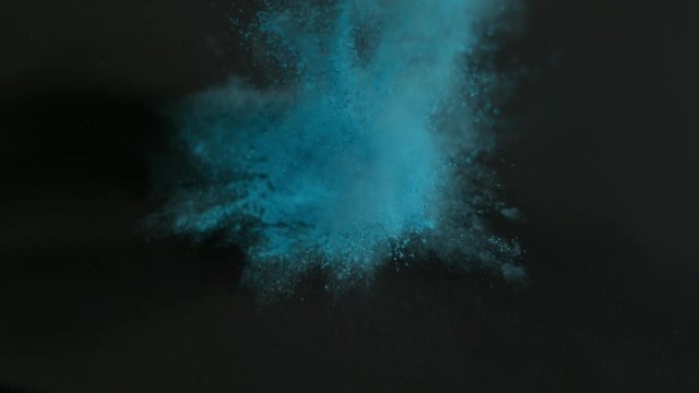 Blue holi powder bounces off black canvas, slow motion closeup