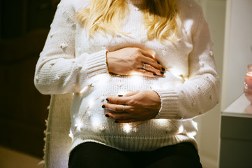 Blonde pregnant woman, whose belly is decorated with fireflies, hugs it