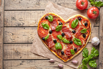 Pizza heart love Valentine's Day romantic Italian restaurant dinner food. Prosciutto, olives, tomatoes, parsley, basil and mozzarella cheese meal on vintage wooden table