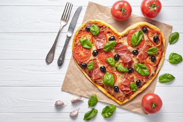 Heart shaped pizza love concept Valentine's Day symbol romantic dinner Italian homemade baked food. Prosciutto, olives, tomatoes, basil and mozzarella cheese meal served on white wooden table