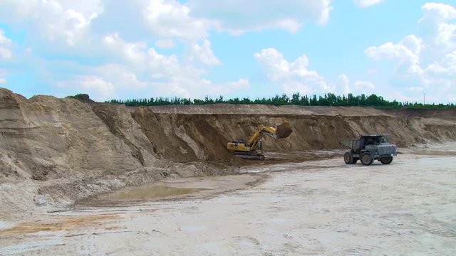 Yellow excavator pours soil into the truck, chalk sand pit
