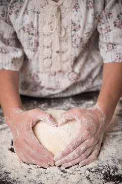 Female hands hold the dough in the shape of heart