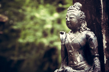 Old Asian style religious sculpture outdoors in the garden with blurred green forest background and copy space in vintage style 