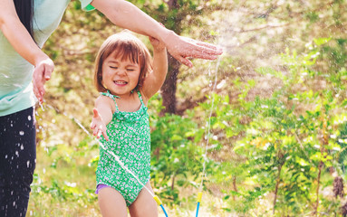 Toddler girl playing in a sprinkler with her mother