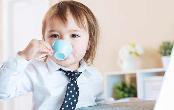 Toddler girl drinking from a mug in front of a laptop
