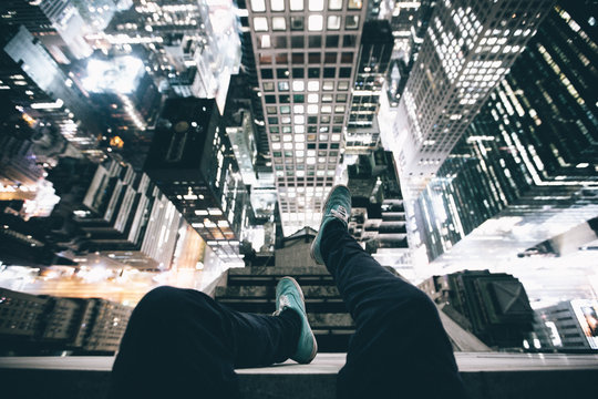 Point of view image of persons legs on top of skyscraper illuminated at night