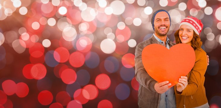 Composite image of happy young couple holding heart shape paper
