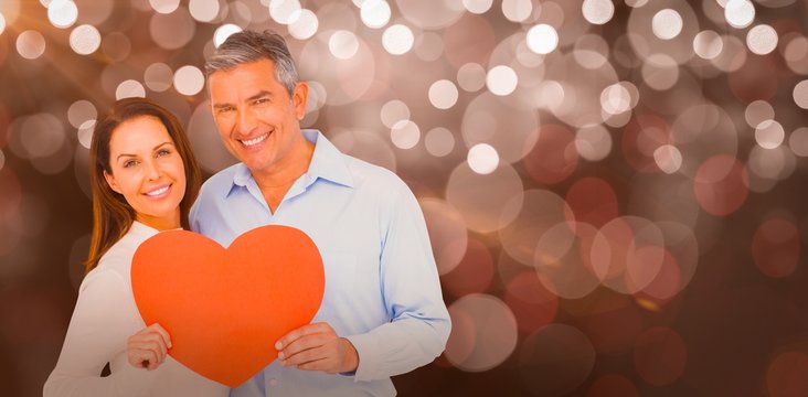 Composite image of happy couple holding big heart shape paper