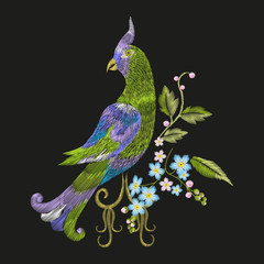 Obraz premium Embroidery colorful floral pattern with fantasy parrot. Vector trend folk green bird with flowers ornament on black background.