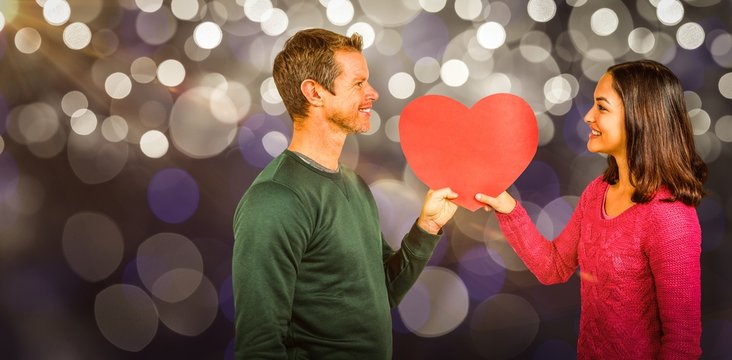Composite image of smiling couple holding red heart shape 