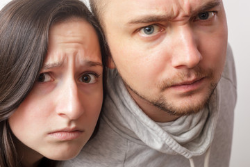 Young couple with dubious looks forward, wrinkling faces