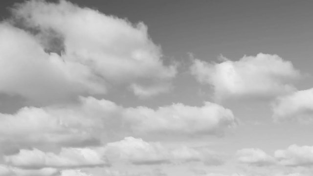 Fluffy clouds move across the sky in this thirty second looping video with a gray tones.