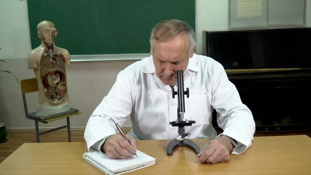 A college professor taking notes and working with microscope in the classroom