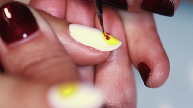 Manicure procedure female hand drawing yellow emoji on white finger nail polish, close up