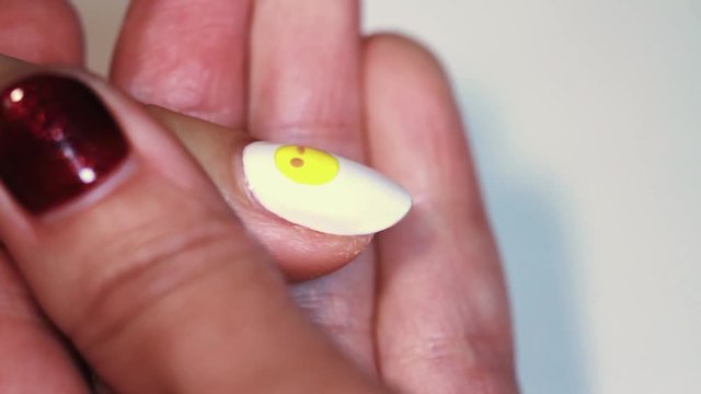 Manicure session female hand drawing yellow emoji on white finger nail polish, close up