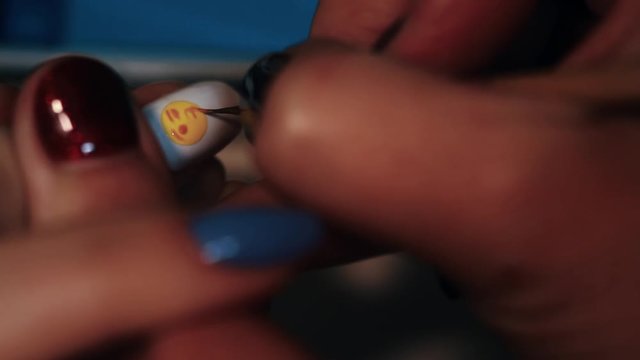 Manicure procedure woman hand painting yellow emoticon on white finger nail polish, close up