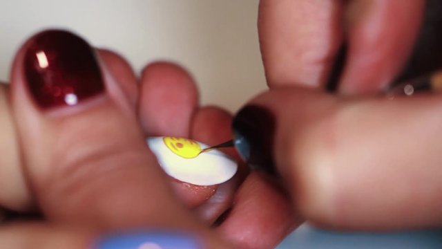 Manicure session woman hand painting yellow emoticon on white finger nail polish, close up