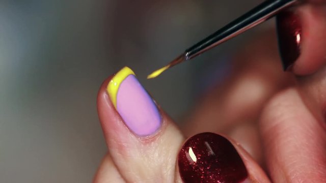 Manicure procedure female hand drawing yellow stripe on purple finger nail polish, close up