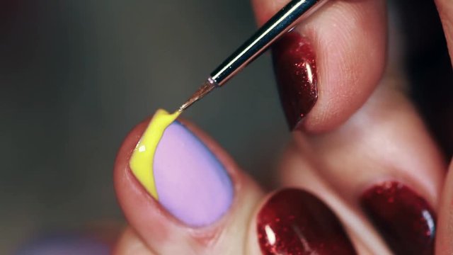 Manicure procedure woman hand painting yellow stripe on purplefinger nail polish, close up