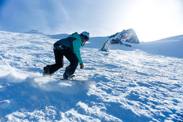 Young woman in teal jacket and white helmet snowboards down a steep mountain - obrazy, fototapety, plakaty