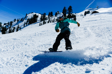 Fototapeta na wymiar Young mixed race woman wearing teal jacket and white helmet snowboards on a clear blue day