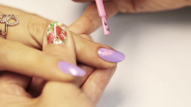 Manicurist hand paints pink finger nail polish on white table in beauty shop, close up